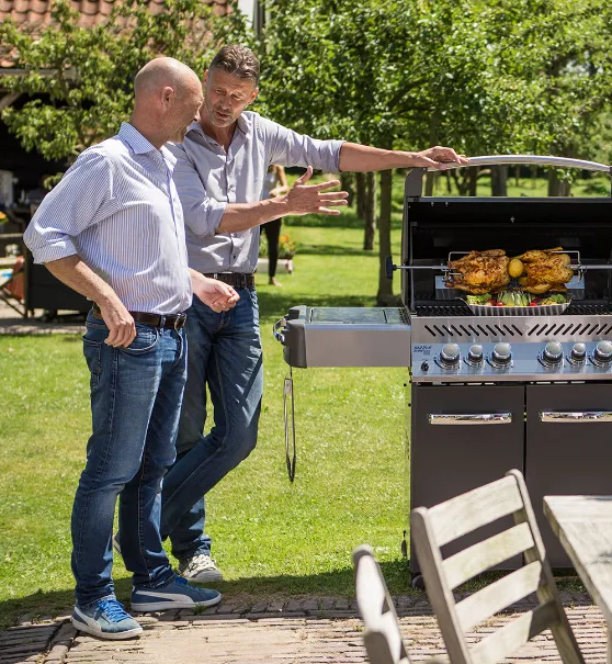 Two men engaging in lively conversation while grilling two chickens on a Napoleon grill