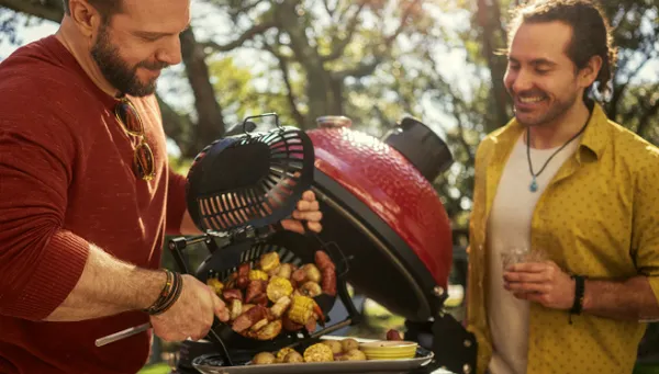 Two smiling men placing potatoes on a Kamado Joe grill