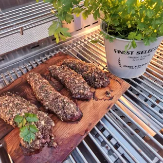 Vier panierte Steaks auf einem Grillrost neben einem Topf mit einer Petersiliepflanze