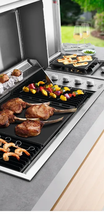 Nahaufnahme eines Grillrosts einer BeefEater Outdoorküche, der reichlich mit Fleisch, Garnelen und Meeresfrüchten belegt ist