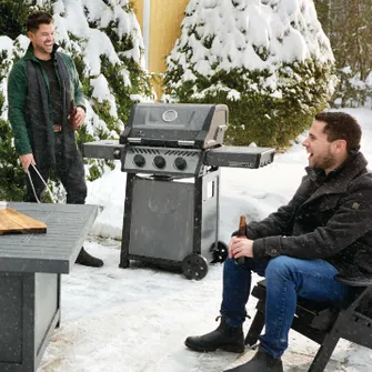 Zwei Männer in Weinterkleidung, die in einem verschneiten Garten grillen