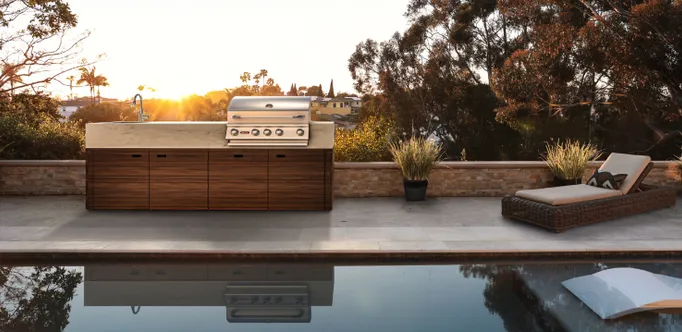 Luxuriöse OCQ Outdoorküche an einem Pool mit Liegestühlen bei Sonnenuntergang